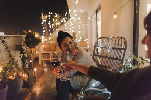Young smiling woman enjoying in good wine and great company on the open terrace of her loft apartment