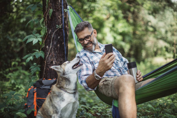 Enjoying nature Mature man at forest. Sitting at hammock and enjoying in nature with his dog. camping photos stock pictures, royalty-free photos & images