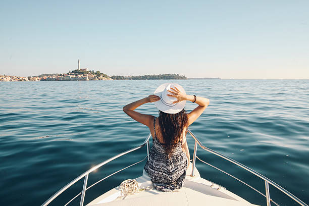 Enjoying summer on the Croatian seaside Young woman enjoys the boatride in the Adriatic sea. The town of Rovigno can be seen on the horizon, and she is wearing a white hat and a dress. Vintage toned leisure, luxury, tourism, carefree concept in the summertime.  nautical vessel photos stock pictures, royalty-free photos & images