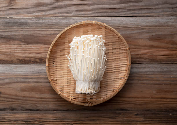 Enoki mushrooms in a bamboo colander set against a wooden background. Enoki mushrooms in a bamboo colander placed against a wooden background. Viewed from above. enoki mushroom stock pictures, royalty-free photos & images