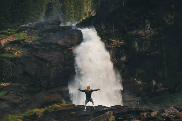 Enormous power of the lower stage Krimml Waterfalls, which shows the power of water. A man stands on the edge of a rock and balances with the resistance of the wind from this waterfall. Austrian water stock photo