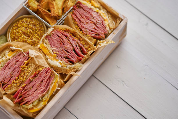 Enormous sandwiches with pastrami beef in wooden box. Served with baked potatoes, pickles stock photo