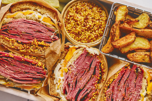 Enormous sandwiches with pastrami beef in wooden box. Served with baked potatoes, pickles stock photo