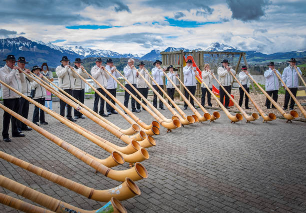 Ensemble of Swiss alphorn blowers are playing outdoor for everyone Avry-devant-Pont, Switzerland - April 27, 2019: Ensemble of Swiss alphorn (alpenhorn, alpine horn) blowers are playing outdoor for everyone. Alphorn is a symbol of Swiss alpine traditions alpine climate stock pictures, royalty-free photos & images