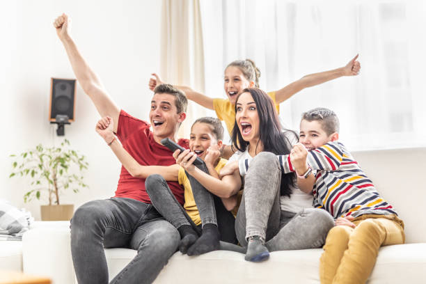 Enthusiastic family of five cheers at home watching sports on TV stock photo