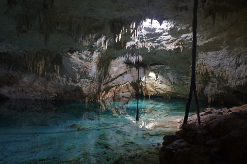 dark entry into underground freshwater cave, with light source, stalactites, and blue water