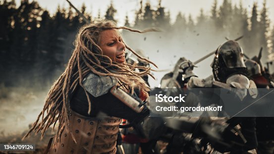 istock Epic Battlefield: Powerful Female Warrior Attacking, Fighting with Sword, Hitting Enemy with Deadly Blows. Dark Age Medieval Battle of Knight Soldiers. Cinematic Historic Reenactment. 1346709124