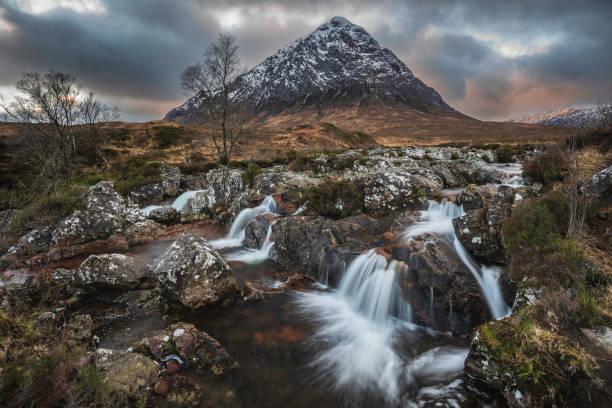 Epic majestic Winter sunset landscape of Stob Dearg Buachaille Etive Mor iconic peak in Scottish Highlands with famous River Etive waterfalls in foreground stock photo