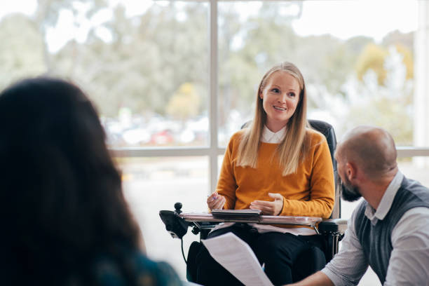 Equal Opportunities in Business A woman looks happy and confident as she leads a group discussion at her place of work. She is a wheelchair user and has Muscular Dystrophy. wheelchair stock pictures, royalty-free photos & images