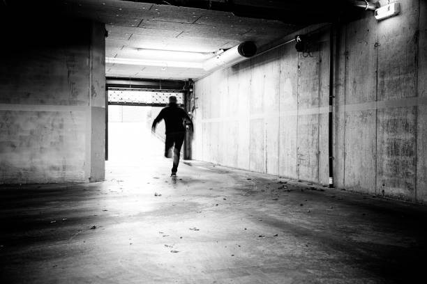 Escaping an underground parking. Monochrome of a man fleeing a grungy underground parking. escaping stock pictures, royalty-free photos & images