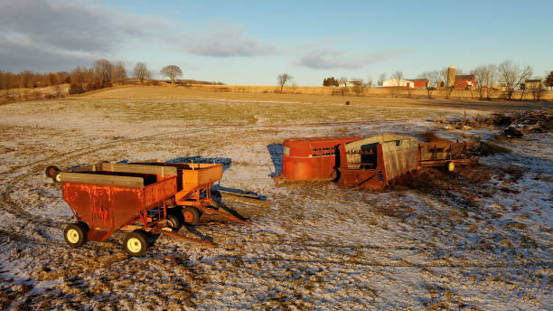 Establishing shot of Midwestern farm in winter. Wagons, agricultural field covered in first snow in the foreground, red barns in the background. Aerial view of American countryside landscape  michigan shooting stock pictures, royalty-free photos & images