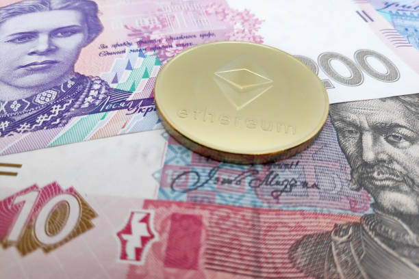Ethereum coin on top of a stack of Ukrainian Hryvnia Close-up on a golden Ethereum coin on top of a stack of Ukrainian Hryvnia banknotes.  With Ethereum  stock pictures, royalty-free photos & images