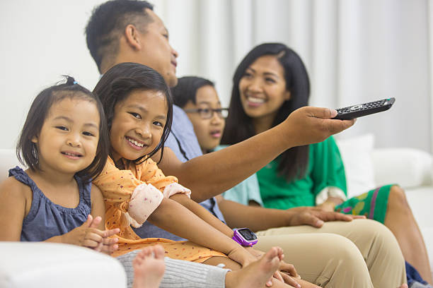 Ethnic family watching television together Ethnic family watching television together in living room asian kids watching tv stock pictures, royalty-free photos & images