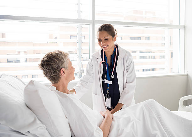 Ethnic female consultant smiling and talking with patient Senior woman in hospital bed listening to attractive female doctor. Medical professional caring for female patient in hospital bed. hospital ward photos stock pictures, royalty-free photos & images