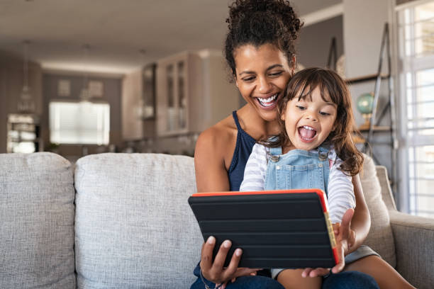 Ethnic mother and little girl having fun with digital tablet Young black mother and smiling daughter playing on digital tablet at home with copy space. Young african american woman with cheerful and excited little girl using digital tablet while relaxing on couch at home. excitement photos stock pictures, royalty-free photos & images