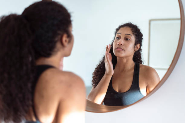 Ethnic woman applies suncream while looking in circular shape mirror Ethnic woman applies suncream before going on a long run. She is wearing active wear. imperfection stock pictures, royalty-free photos & images