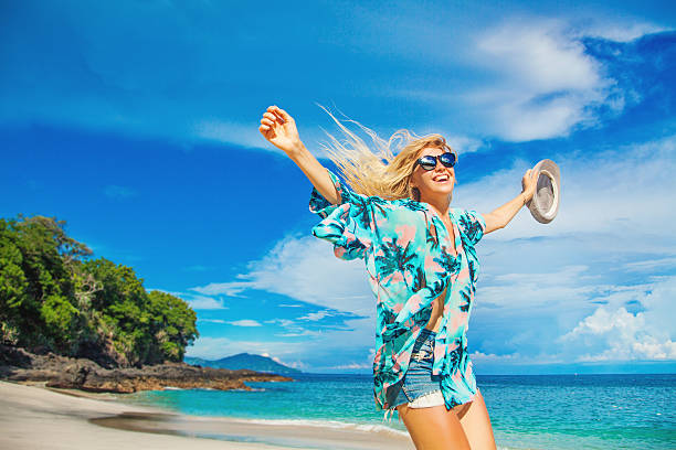 European blond girl jumping on a background of tropical beach beautiful women in hawaiian shirt and jeans shorts jiumping on a background of tropical beach big island hawaii islands stock pictures, royalty-free photos & images