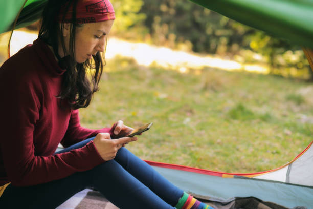 European woman in a tent overlooking the forest  holds a telephone in her hands. A modern holiday with devices and the Internet, to be always in touch on vacation and vacation. stock photo