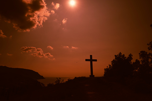 Evening landscape. The Cross of God on the hill in cloudy weather. A picture on a warm orange sunset day