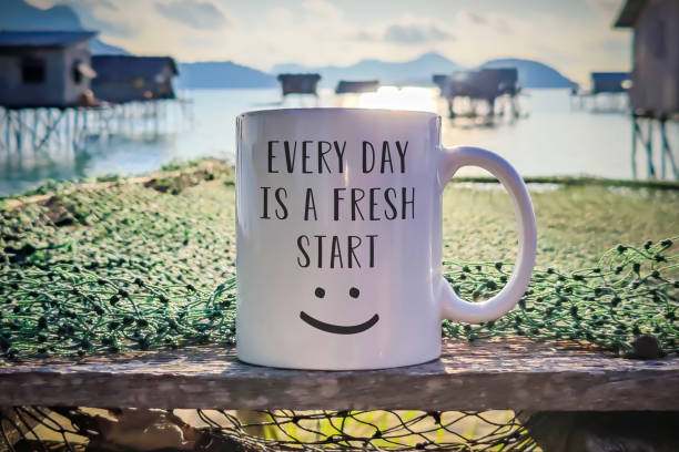 "Every day is a fresh start" text with a happy smile on a cup of morning coffee with sea background. stock photo