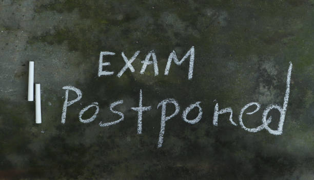 Exam Postponed Written on Blackboard with White Chalk Exam Postponed Written on Blackboard with White Chalk in Horizontal Orientation. Exam Cancellation or Postponed Conceptual Photo. postponed stock pictures, royalty-free photos & images