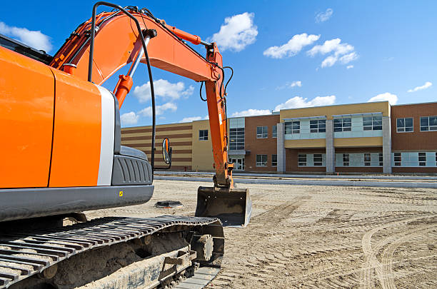 Sebuah excavator konstruksi oranye terang di tempat parkir baru-baru ini dinilai dari sekolah menengah baru. Gambar Serupa: