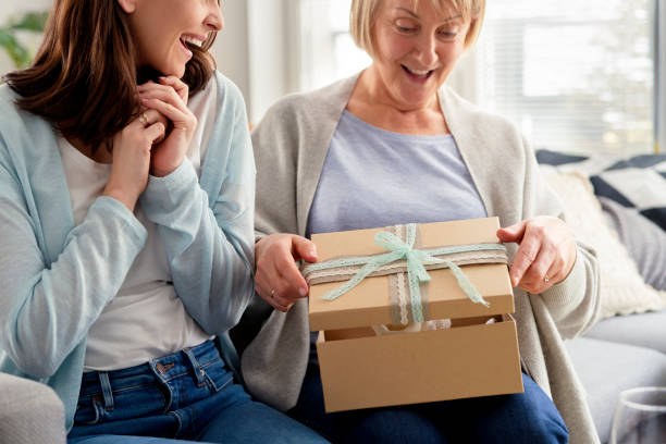 Excited adult daughter waiting for mom to open the gift stock photo