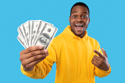 Big Financial Success. Excited African Guy Showing Dollar Money Cash Over Blue Studio Background. I'm Rich. Profit And Income, Abundance Concept. Selective Focus