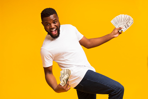 Excited African Man Holding Plenty Of Money On Yellow Background