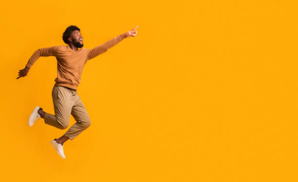 Excited black guy running towards copy space Magnetic offer. Excited afro man pointing and running towards copy space, orange studio background jumping stock pictures, royalty-free photos & images