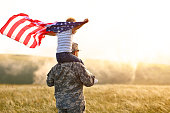istock Excited child sitting with american flag on shoulders of father reunited with family 1333389184