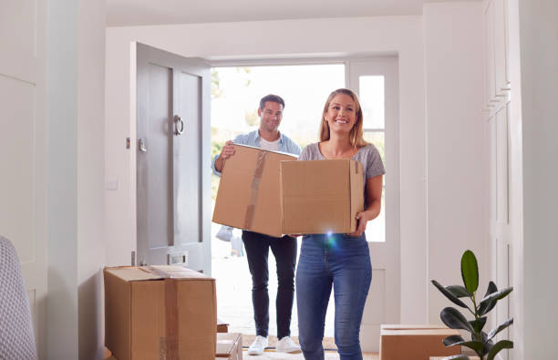 Excited Couple Carrying Boxes Through Front Door Of New Home On Moving Day stock photo