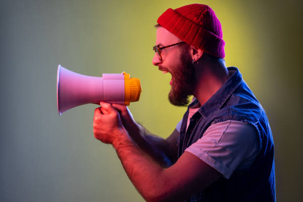 Excited crazy bearded hipster man screaming holding loudspeaker megaphone, looking to left side. stock photo