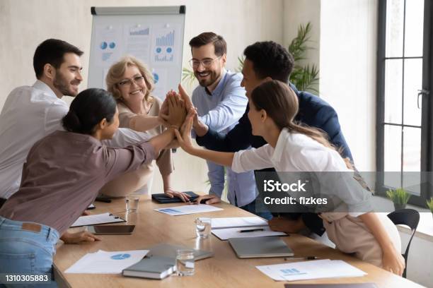 Excited diverse employees give high five at meeting