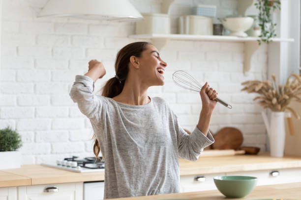 Excited funny girl singing into whisk, having fun in kitchen Excited funny girl singing into whisk, having fun in modern kitchen at home, happy girl holding beater as microphone, dancing, listening to music, having fun with kitchenware, preparing breakfast singing stock pictures, royalty-free photos & images