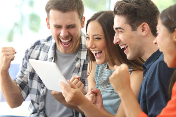 Excited group of friends watching tv from tablet Excited group of four friends viewing media content on line from a tablet in a house interior exam success stock pictures, royalty-free photos & images