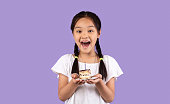 紫色の背景の上に誕生日ケーキを保持している興奮した日本の子供の女の子