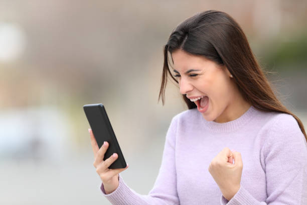 Excited teen reading phone content in the street Excited teen reading phone content in the street scholarships for females stock pictures, royalty-free photos & images