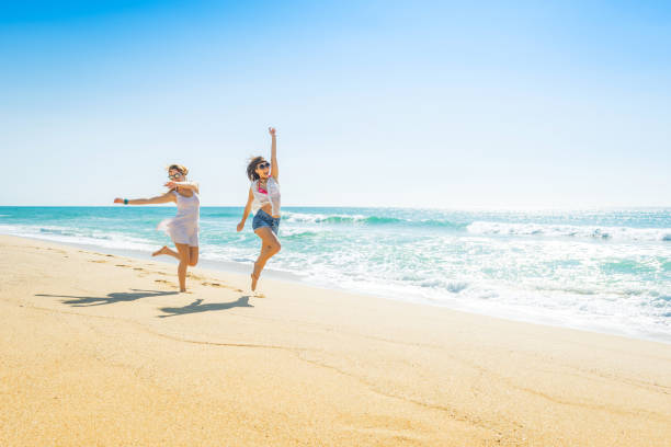 Excited trendy young friends jumping and running on the beach stock photo