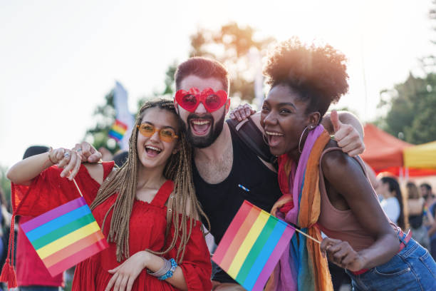 Excited young people meeting at the pride festival Young beautiful people celebrating the pride event, hugging, waving rainbow pride flags and having fun gay pride symbol stock pictures, royalty-free photos & images