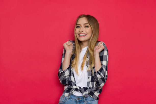 Excited Young Woman Is Smiling. An excited young woman is gesturing and smiling. Waist up studio shot on red background. plaid shirt stock pictures, royalty-free photos & images