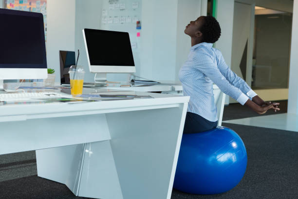 Executive exercising on fitness ball Executive exercising on fitness ball in futuristic office yoga ball work stock pictures, royalty-free photos & images