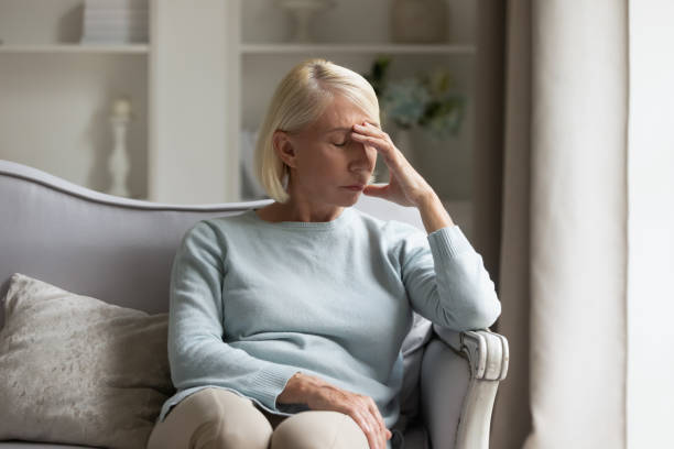 Exhausted mature lady suffering from head ache at home. Tired older woman sitting on comfortable sofa in living room, touching forehead. Exhausted mature lady suffering from head ache at home. Unhappy elder grandmother worrying about bad news alone. chronic illness stock pictures, royalty-free photos & images