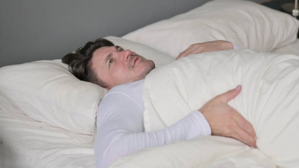 hombre de mediana edad agotado con dolor de espalda acostado en la cama - back pain when sleeping fotografías e imágenes de stock