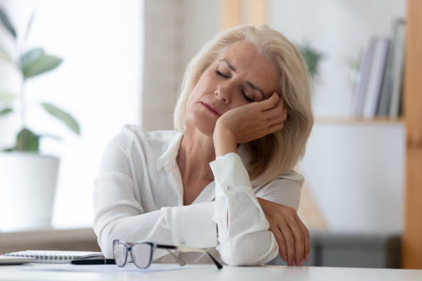 mujer de negocios senior agotada quese duerme en el lugar de trabajo - agotamiento fotografías e imágenes de stock
