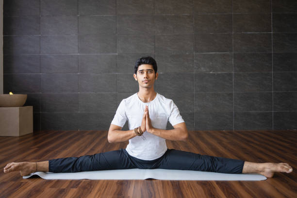 Experienced Indian yogi doing splits in gym Experienced Indian yogi doing splits in gym. Man looking at camera, holding hands together and practicing yoga. Yogi concept. Front view. doing the splits stock pictures, royalty-free photos & images