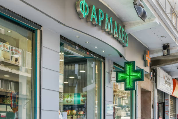 External day view of Hellenic pharmaceutical shop with illuminated green cross. stock photo