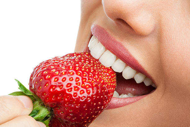 Extreme close up of teeth biting strawberry. stock photo