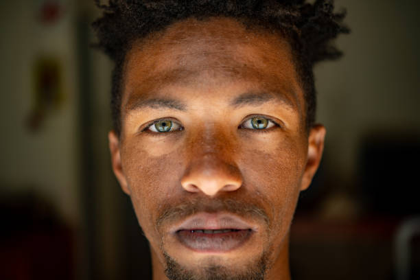 Extreme Close up Serious Headshot Landscape Portrait of young mixed race male face with green eyes facial hair and rasta hair stock photo