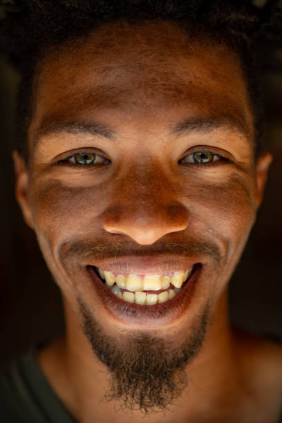 Extreme Close up Smiling Headshot Portrait of young mixed race male face with green eyes facial hair and rasta hair stock photo